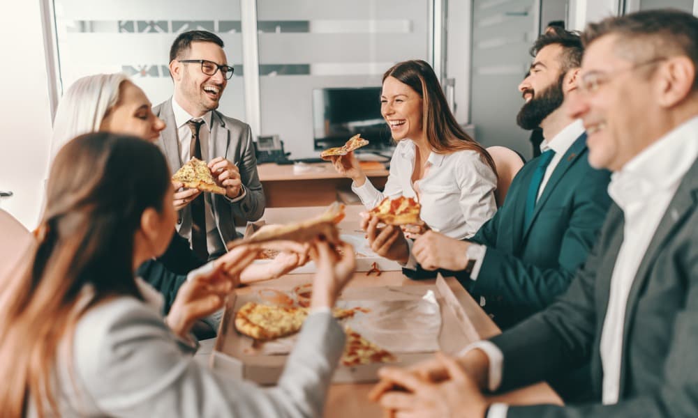 a group of employees enjoying a work-life balance in the office by gathering for pizza